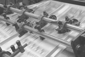 A close-up of a printing press in operation, enhanced by Onyx Graphics RIP Software, with sheets of paper moving quickly under roller bars.