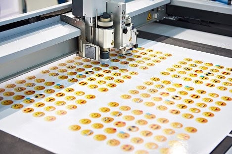 A digital cutting machine is processing a sheet of printed emoji stickers arranged in rows on a flat surface, seamlessly integrated with Onyx Graphics RIP software for precise cutting.
